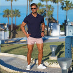man wearing stylish smart casual outfit with navy blue slim fit polo and very short shorts in light pink
